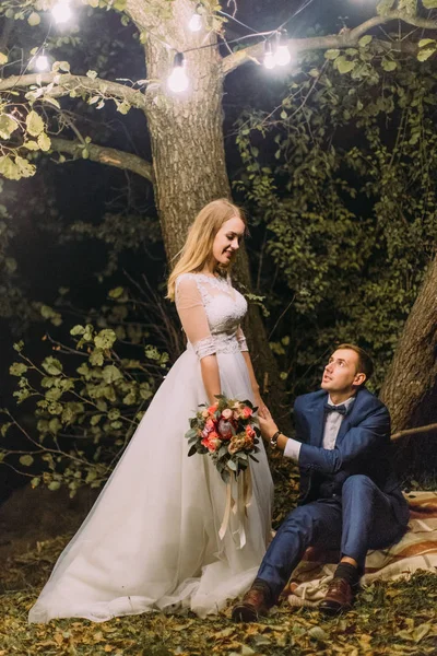 ガーランド ランプで飾られたツリーの下の花嫁の手を握って新郎の素敵な肖像画. — ストック写真