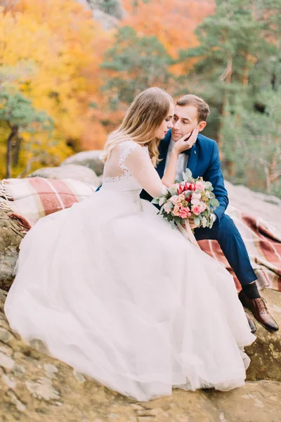 坐在岩石上的新婚夫妇的垂直照片。新娘抚摸着新郎的脸颊。. — 图库照片
