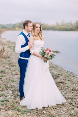 Damat güzel gelin buketi arka ile sarılma ve deniz manzarası izlerken.