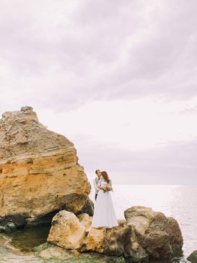 Damadın gelini geri sarılma ve onu deniz arasında Uçurumdaki dururken kafasına öpüşme tam uzunlukta görünümü.