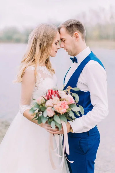 Retrato lateral sensível dos recém-casados de pé frente a frente com o buquê de casamento . — Fotografia de Stock