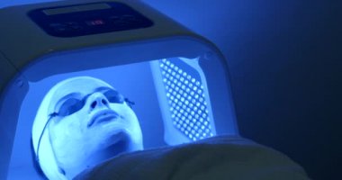 Maske ve gözlük rahat kadınla yüz için led ışık tedavisi görüyor. Spa salonu konumu. 4 k görüntüleri.