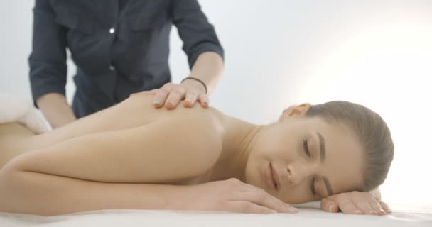 Handen van de vrouwelijke massager doen de rug massage voor mooie jonge vrouw met gezonde porselein huid en natuurlijke make-up. 4 k-beeldmateriaal. — Stockvideo