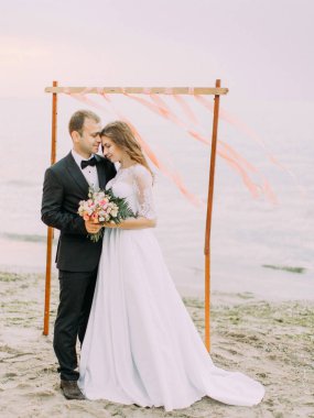 Kafa kafaya sahilde pembe kurdele ile süslenmiş arch önünde duran yeni evlilere harika tam uzunlukta manzara.