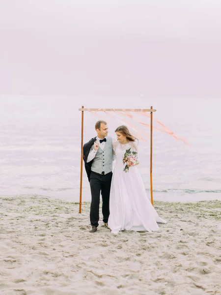 Felices recién casados caminando por la playa durante el atardecer . —  Fotos de Stock