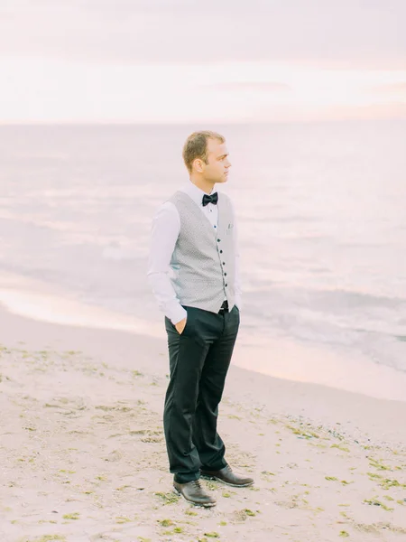 La vista laterale a tutta lunghezza dello sposo vestito con il papillon nero sullo sfondo del mare . — Foto Stock