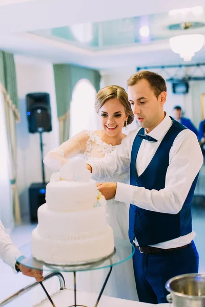 Recém-casados alegres cortando sua primeira parte do bolo de casamento . — Fotografia de Stock