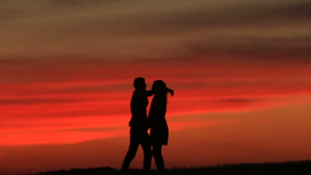 Siluetas de la hermosa pareja feliz besándose suavemente sobre la puesta de sol roja . — Vídeo de stock
