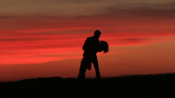 Silhouettes of the adorable couple tenderly kissing while dancing over the red sky during the sunset. — Stock Video