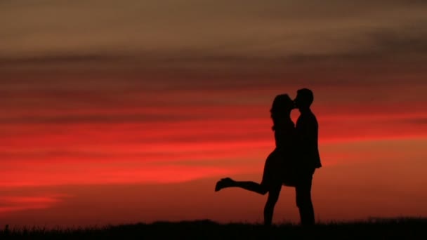 Full-length view of the couple silhouettes softly kissing over the red sky during the sunset. Romantic atmosphere.