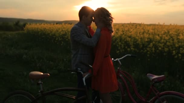 Çiçek açan alanındaki Bisiklet yakınındaki günbatımı sırasında sarılma duyarlı çift romantik portresi. Adam şefkatle sevgilisi yüzünü okşayarak. — Stok video