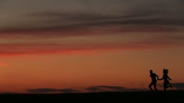 Mutlu çiftin elele ve aktif olarak çalışıyor ve parlak güneşin atlama sırasında eğlenmek siluetleri