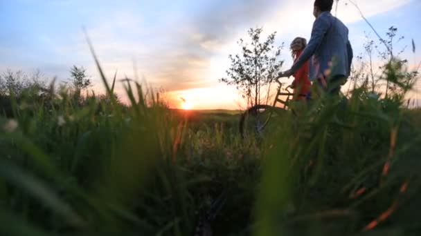 De lachende gelukkige paar loopt met fietsen langs de prachtige bloeiende veld tijdens de heldere kleurrijke zonsondergang. Zijaanzicht. — Stockvideo