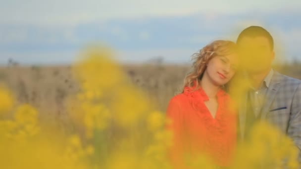 Retrato de cerca de la hermosa pareja pacífica abrazándose tiernamente mientras disfruta de la vista de la naturaleza del floreciente campo amarillo. Se miran a los ojos. . — Vídeos de Stock