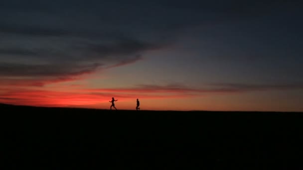 Silhouttes de la feliz pareja que corre. El hombre está corriendo detrás de su amante mujer sobre el cielo brillante y colorido . — Vídeo de stock