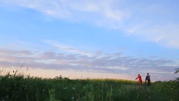Caminhada romântica de dois amantes adoráveis com bicicletas no belo campo verde sobre o belo céu . — Vídeo de Stock