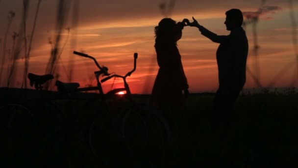 Sensible pareja de amantes bailando en el campo sobre el rojo brillante atardecer. Vista completa de las siluetas. Caminar con bicicletas . — Vídeos de Stock