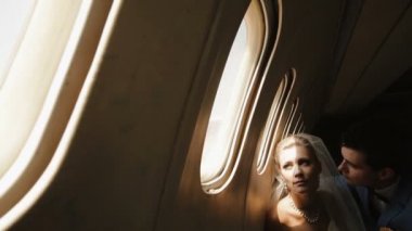 Yakın çekim yakışıklı damat büyüleyici gelini uçağın penceresinde yanında otururken yanak içinde öpüşme portresi.