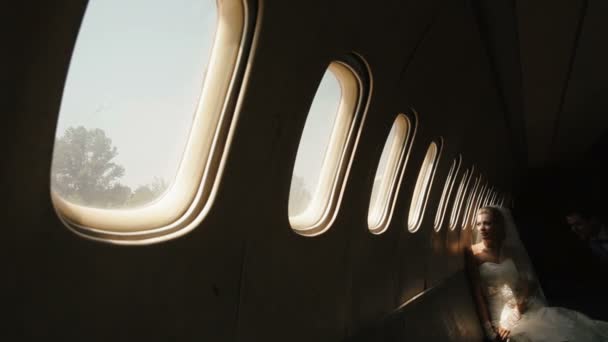Uma atmosfera romântica. noiva loira bonita está olhando jogar a janela no avião, enquanto o noivo está beijando-a na bochecha . — Vídeo de Stock