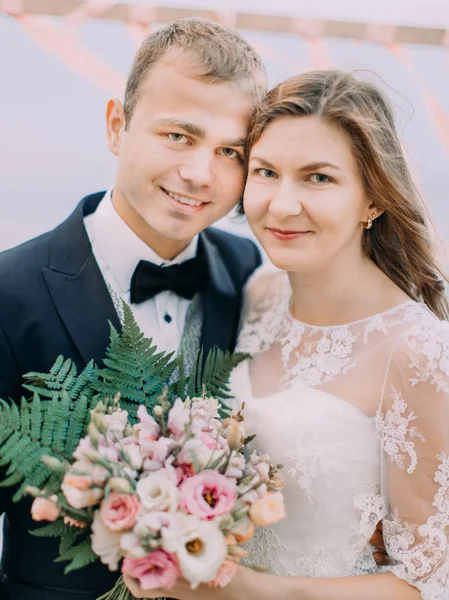 Il ritratto ravvicinato degli sposi sorridenti. La sposa sta tenendo il bouquet di nozze costituito da rose bianche e rosa . — Foto Stock