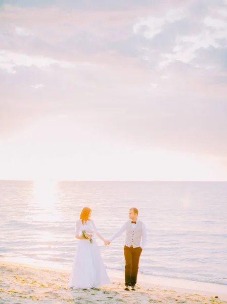 A séta során a naplemente a strandon a boldog newlywed pár. A pár a kézen. — Stock Fotó