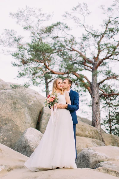 Damat Gelin kaya üzerinde dururken yanak içinde öpüşme romantik tam uzunlukta bakış. — Stok fotoğraf