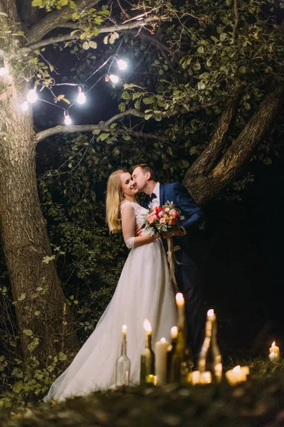 Damat öpüşme mutlu gelin mumları şişelerde arkasında tam uzunlukta fotoğraf. Gece kompozisyon. — Stok fotoğraf