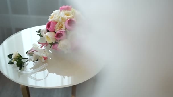 Hermoso ramo de boda de rosas rosadas y blancas y encantadores boutonnieres coloridos están acostados en la mesa blanca . — Vídeos de Stock