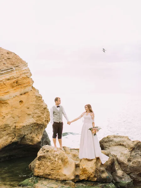 A kezemet a sziklafalon a háttérben a tenger newlywed pár függőleges fénykép. — Stock Fotó