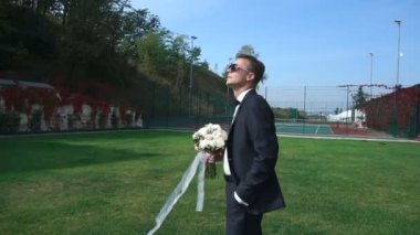 Gül buketi çiçek açan bahçede tutan güneş gözlüğü ile kamera yakışıklı çekici damat etrafında çember.