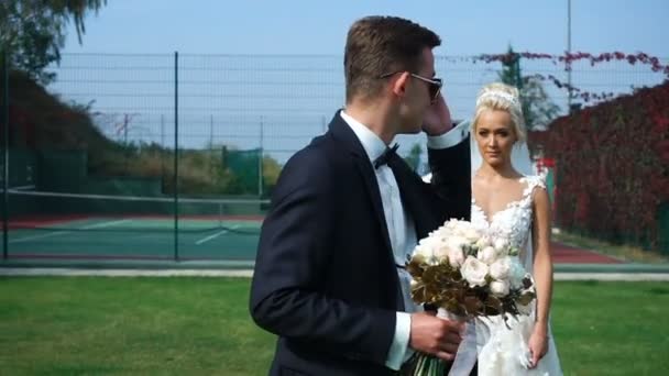 Charmante mariée blonde vient à son beau marié avec un boquet de roses. Rencontre des jeunes mariés dans le jardin fleuri . — Video