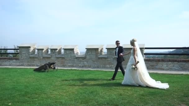 Elegante pareja de recién casados en amante están tomados de la mano y bailando mientras caminan por el floreciente jardín cerca del antiguo castillo . — Vídeos de Stock