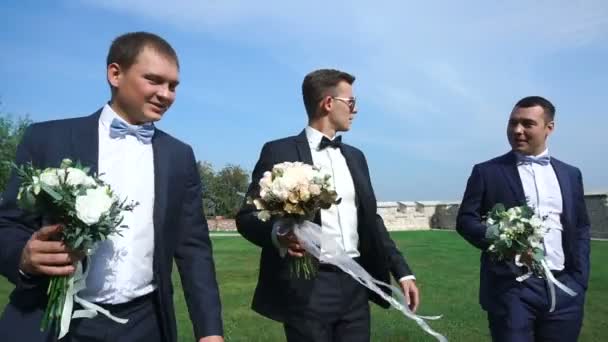 Novio guapo y sus mejores hombres con ramos de boda están caminando por el jardín y hablando . — Vídeo de stock