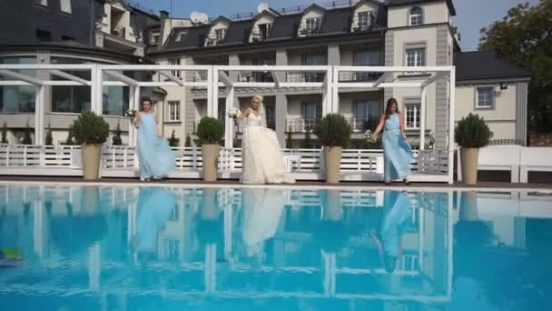 Jovem noiva encantadora está se divertindo com suas amigas enquanto dança perto da piscina de luxo. Dia do casamento . — Vídeo de Stock