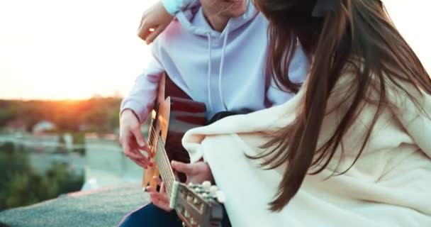 Ritratto romantico della bella coppia felice avvolta in un plaid e teneramente abbracciata mentre si siede sul tetto. Il bell'uomo suona la chitarra . — Video Stock