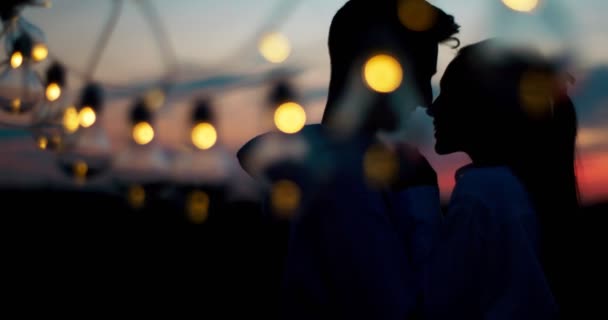 Retrato romántico de las siluetas de dos amantes. El tipo está besando las manos de su amante mientras está de pie detrás de la cadena de luces. Imágenes de 4k . — Vídeos de Stock