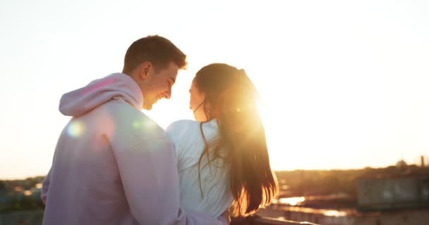 Vista trasera de cerca de la feliz pareja atractiva abrazándose tiernamente y disfrutando de la puesta de sol. El chico guapo está besando a su amante en la mejilla . — Vídeo de stock