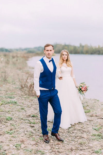 Celovečerní pohled ženich vede nevěstu podél pláže. — Stock fotografie