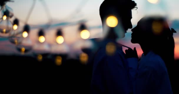 Vista de cerca de la cadena de bombillas. Besar tiernamente a un par de amantes detrás de ellos. Fecha romántica . — Vídeos de Stock