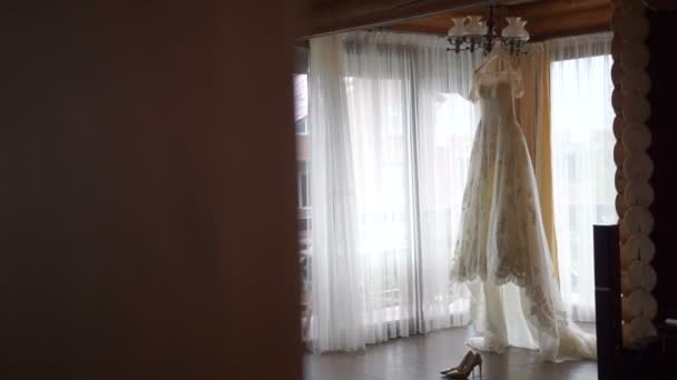 De perfecte witte trouwjurk is opknoping op de hanger in de kamer van de bruid. Elegante hoge hakken liggen in de buurt van de jurk. — Stockvideo