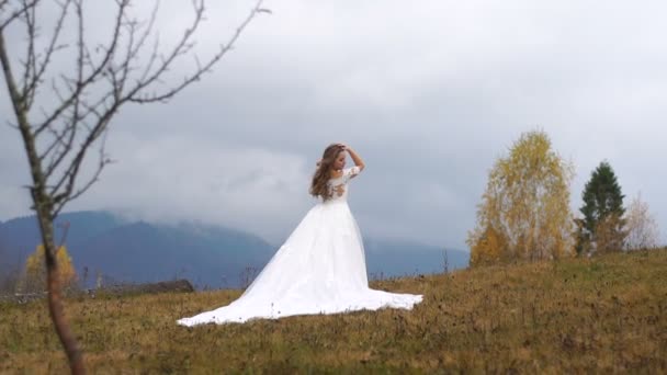 Ganzkörperansicht der bezaubernden Braut im langen Brautkleid, die auf dem Gipfel der Herbstberge posiert. — Stockvideo