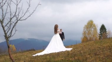 Sonbahar dağların tepesinde duran ve şefkatle onu sarılma moda uzun elbise onun güzel çekici gelin gelen yakışıklı damat tam uzunlukta görünümünü.