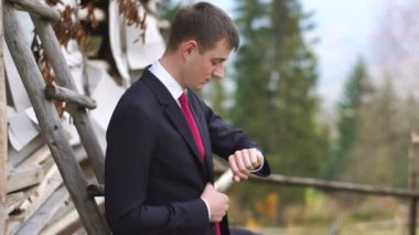 Şık damat üzerinde ahşap ev yaslanmış iken el izle zamanında kontrol ediyor. Köy yürüyor.