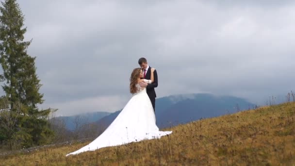 Hochzeitspaar kuschelt sich bei trübem Wetter zärtlich auf den Gipfel der Herbstberge. Ansicht in voller Länge. — Stockvideo