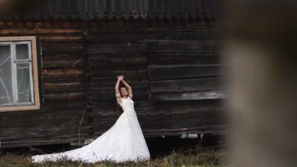 La belle mariée élégante pose près de la vieille maison rustique en bois dans le village . — Video