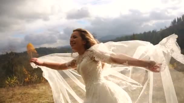 Divertente sposa sorridente è felicemente scuotendo la testa e giocando con il suo velo in soleggiate montagne d'oro . — Video Stock