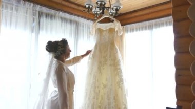 İpek elbise ve peçe saç sevimli gelin askıda asılı beyaz güzel düğün elbisesini bakıyor.