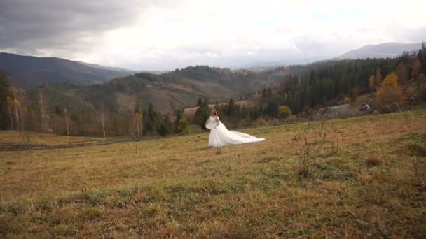 Gorgeous cheerful bride is running along the fantastic meadow. Beautiful nature lanscape of golden mountains. — Stock Video