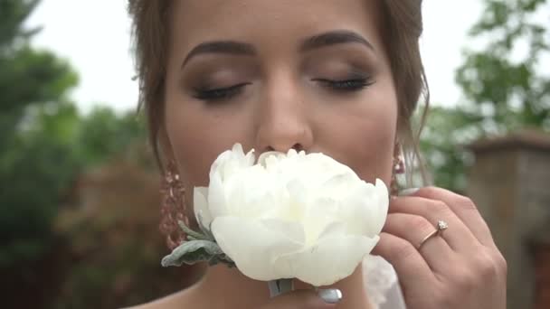 Nahaufnahme Porträt der charmanten Braut mit natürlichem Make-up, die die weiße Pfingstrose mit geschlossenen Augen riecht. — Stockvideo