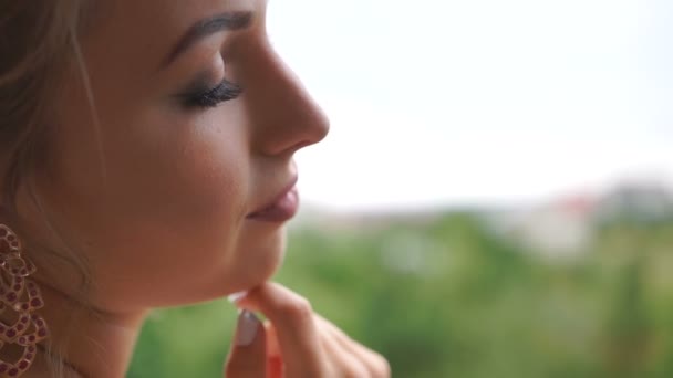 Närbild sida porträtt av aforable blonda bruden med vacker make-up och perfekt slöja tittar genom fönstret. — Stockvideo